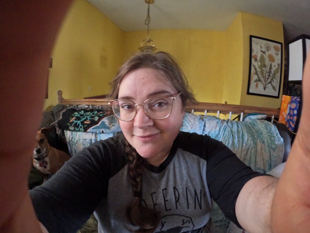 A photo of a femme person in glasses, from the perspective that they are holding the camera and looking back into the lens.